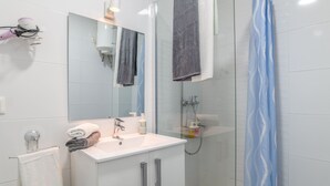 Een moderne badkamer met een douchecabine van glas, een witte wastafel en een spiegel erboven.