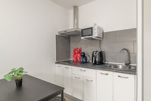 Una cocina compacta equipada con microondas, hervidor y una planta en maceta.