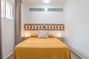 Un dormitorio con una cama, cabecera de madera, mesita de noche y ventana con cortinas.