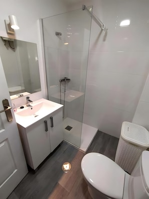 Un bany modern amb dutxa envidrada, un lavabo blanc i un vàter.