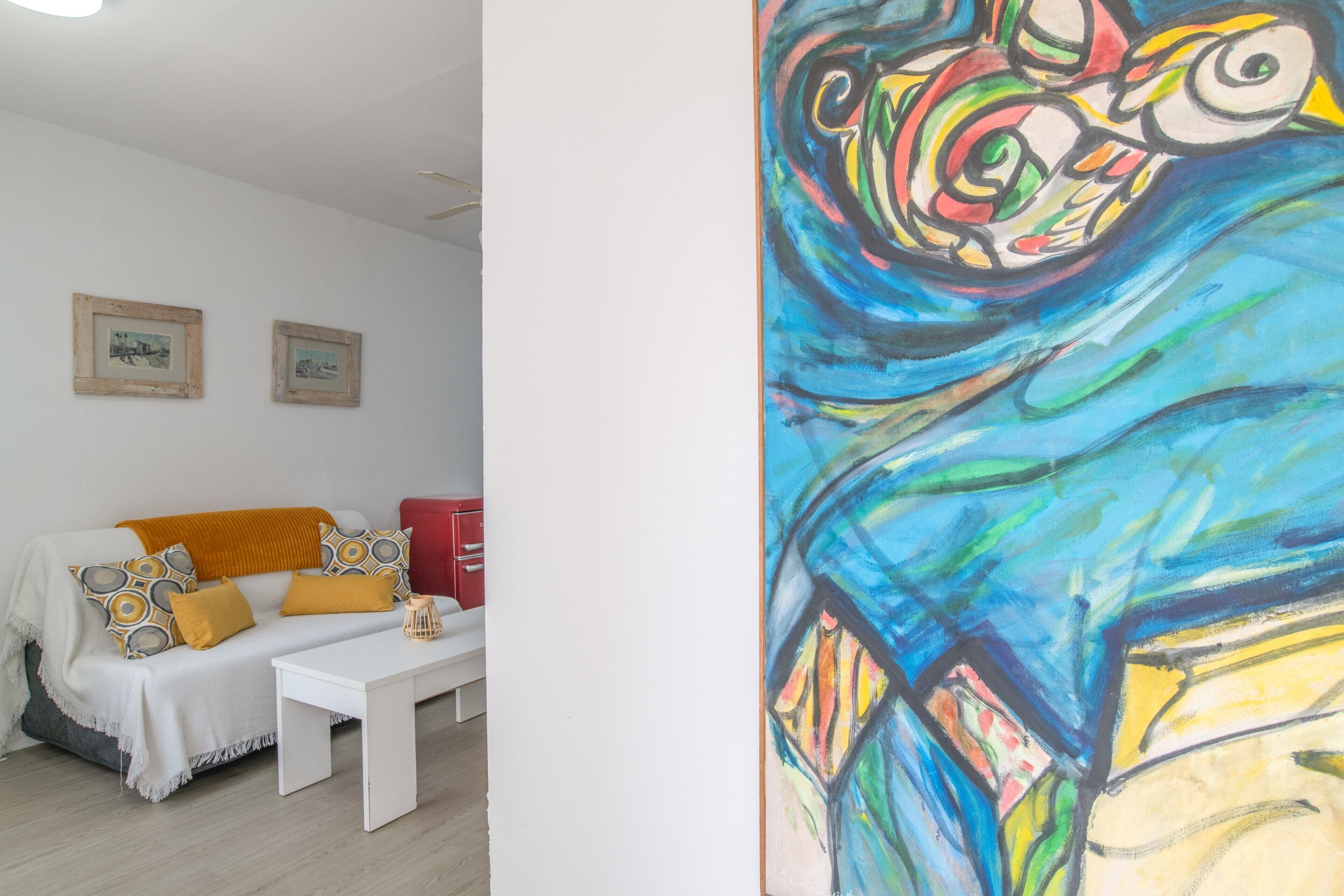 A room with a white sofa, a small white table, and a colorful abstract painting on the wall.
