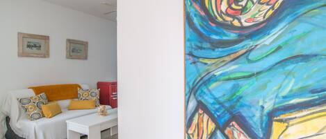 A room with a white sofa, a small white table, and a colorful abstract painting on the wall.