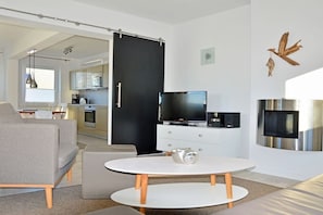 Ein modernes Wohnzimmer mit einer Couch, einem runden Tisch, einem Fernseher und einer Küche im Hintergrund.