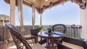 Ein Balkon mit Korbmöbeln, einem Glastisch und hängenden Pflanzen.