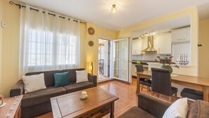 Ein Wohnzimmer mit einer Couch, einem Couchtisch und einem Essbereich mit Stühlen sowie einer Küche im Hintergrund.