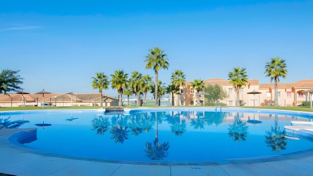 Ein großer Pool im Freien, umgeben von Palmen und Gebäuden, mit blauem Himmel.