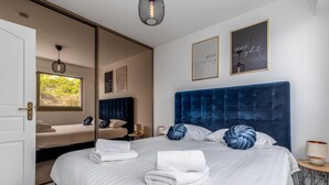 Quarto com uma cama grande, um espelho, uma janela e dois posters motivacionais emoldurados.