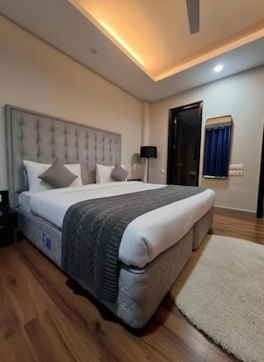 A modern bedroom with a large bed, a ceiling fan, and a door leading to another room. - Giri Prime Inn Cyber City By OTABoostup (Gurugram)