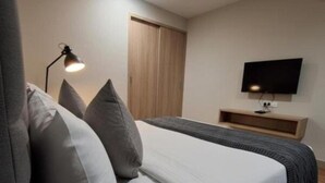 Une chambre à coucher moderne, équipée d’un lit, d’un bureau, d’une télévision et d’un ventilateur de plafond.