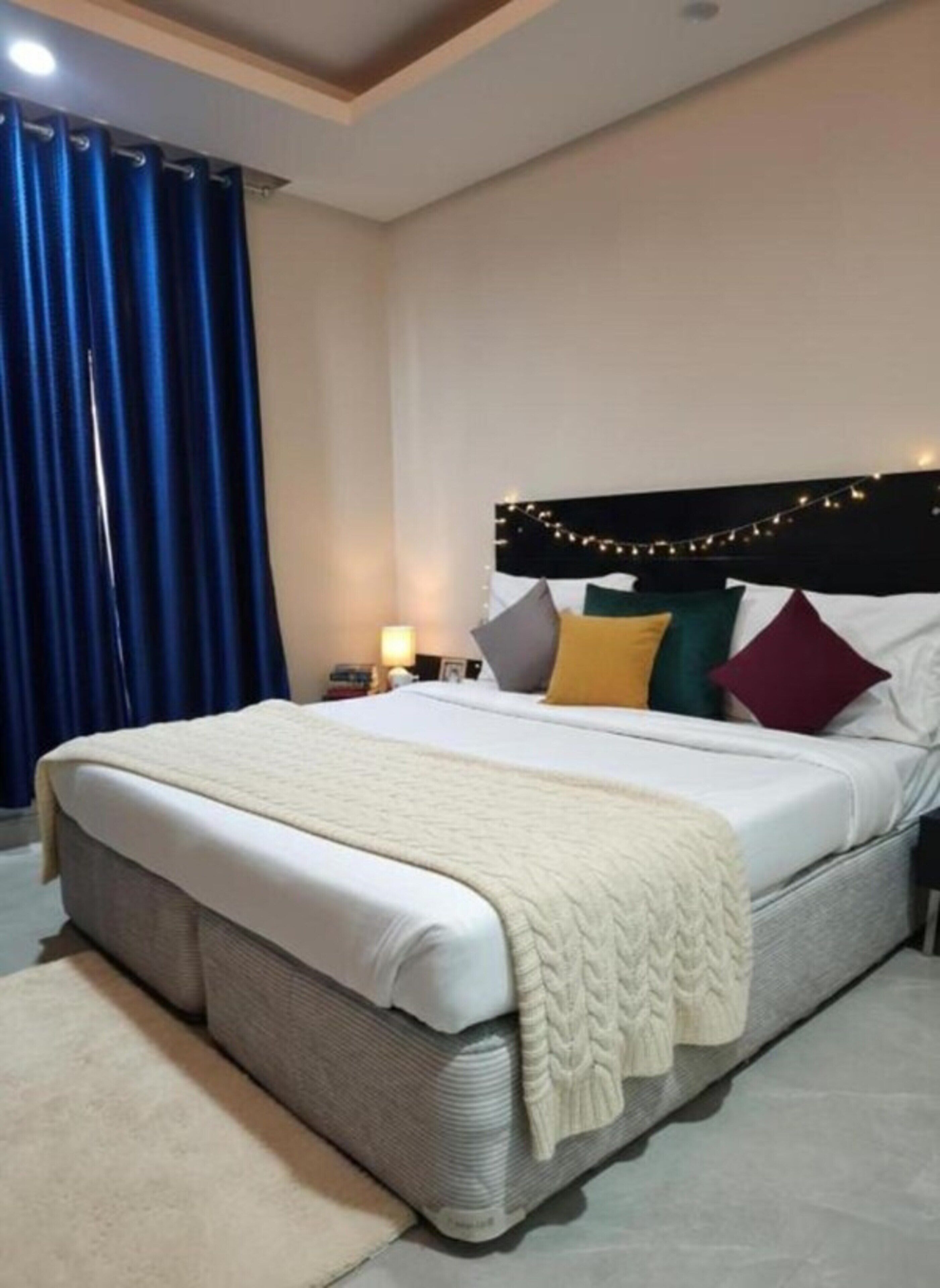 A neatly made bed with a headboard, a bedside table with a lamp, and a blue curtain.