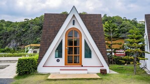 Un bâtiment de forme triangulaire, doté d’une porte centrale, entouré de verdure et ayant une chaîne de montagnes en arrière-plan.