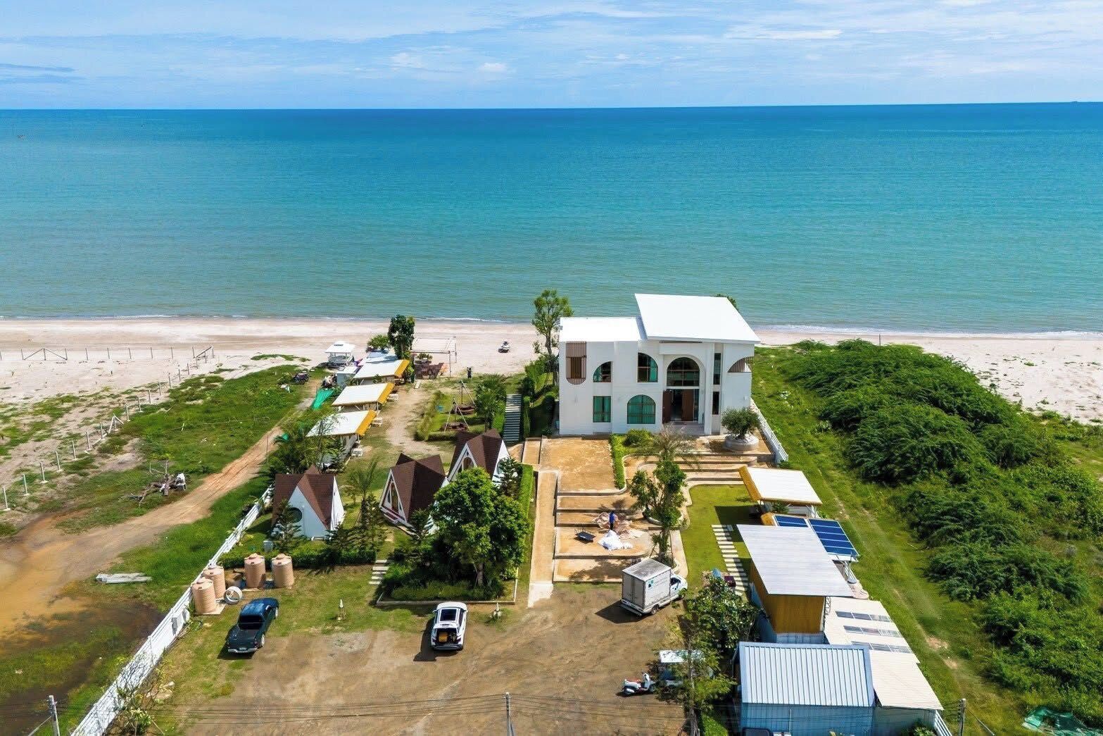 A coastal property with a central white building, a beach, and a parking area.. BanKraJome Magodkan Beach