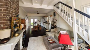 A spacious living area with a high ceiling, a staircase, and a kitchen in the background. - Historic Creole Cottage In The Marigny (New Orleans)