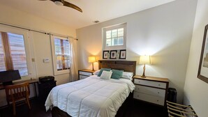 A bedroom with a bed, two bedside tables, a desk, a chair, a ceiling fan, and a window with blinds. - Historic Creole Cottage In The Marigny (New Orleans)