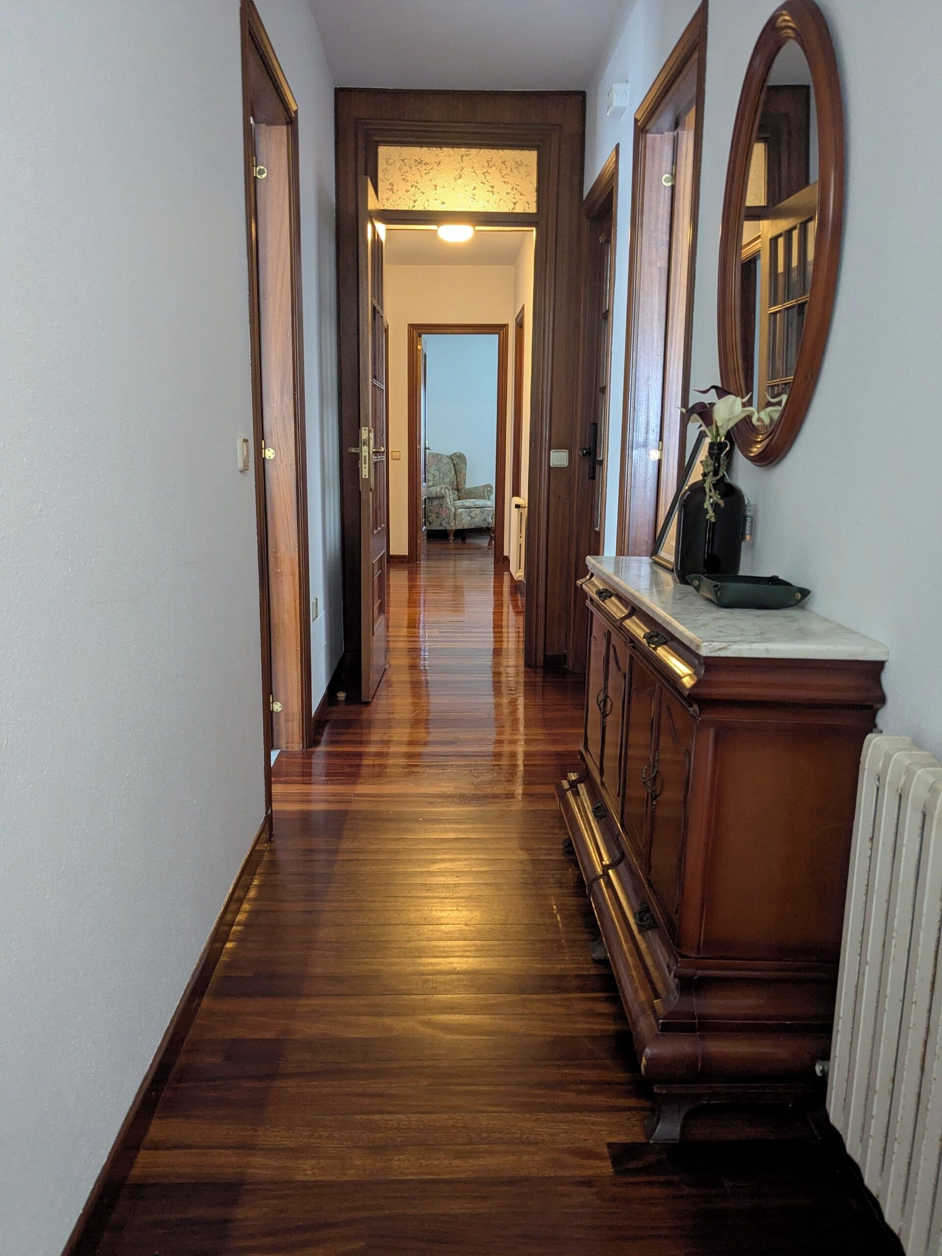 Ein Korridor mit Holzboden, einem Heizkörper und einem Spiegel an der Wand.
