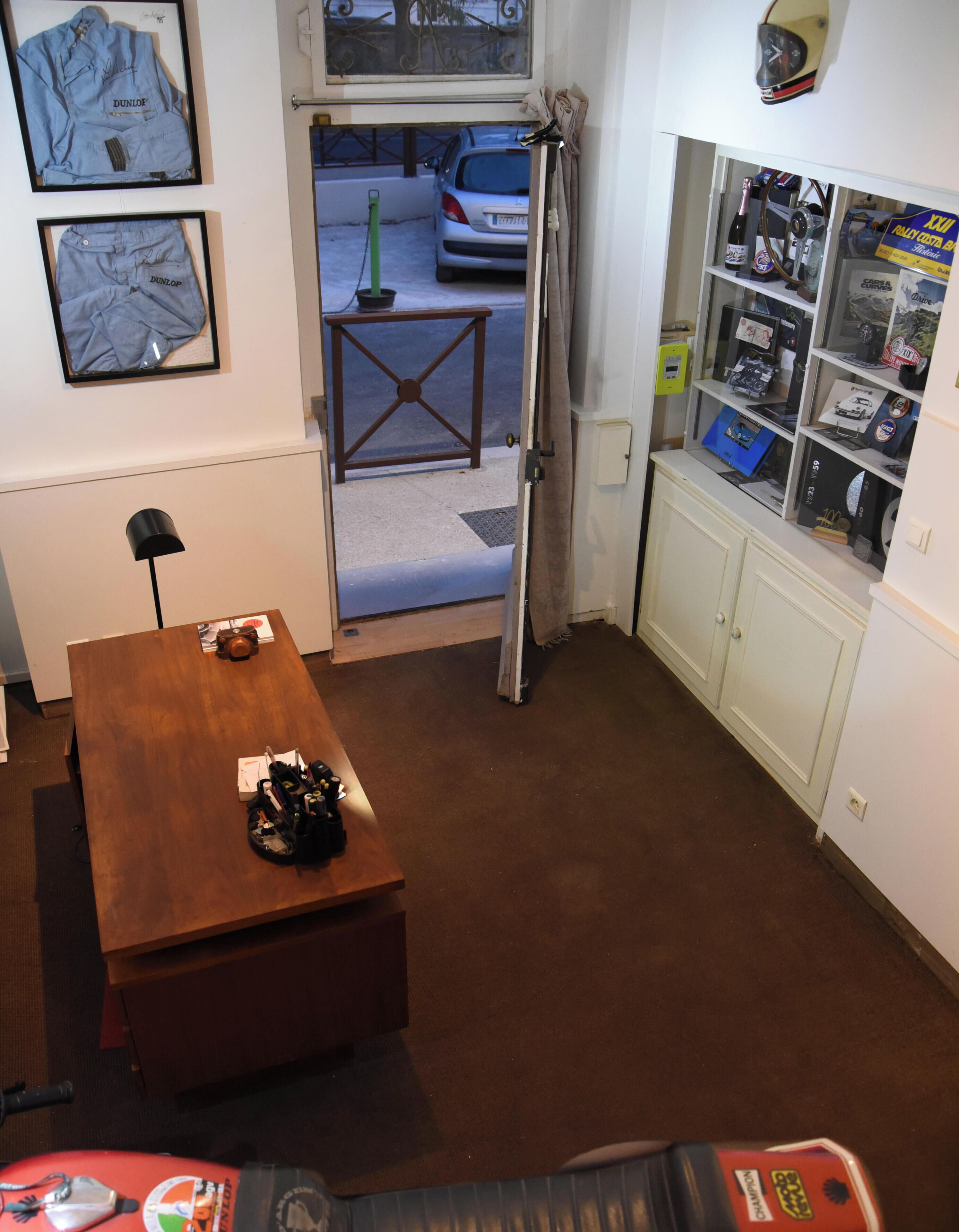 A room with a wooden table, a motorcycle, a door leading outside, and a shelf with various items.