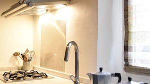 Una cocina con estufa a gas, lavamanos y cafetera.