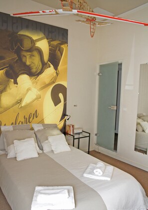 A bedroom with a large bed, a door, a small table, and a wall with a graphic. - Driver's House (Saint-Rémy-de-Provence)