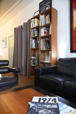 A room with a leather couch, a wooden coffee table, a bookshelf, and a door with curtains. - Driver's House (Saint-Rémy-de-Provence)