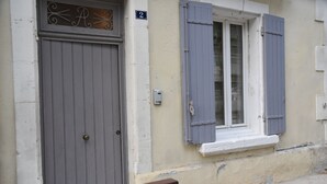 Un edificio con una puerta gris cerrada, una ventana con contraventanas y un pequeño balcón.