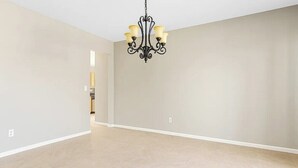 A spacious room with a chandelier, light-colored walls, and a tiled floor.