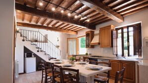 Una cocina con una mesa de comedor para cuatro personas, armarios de madera, una escalera y vistas al exterior con vegetación.