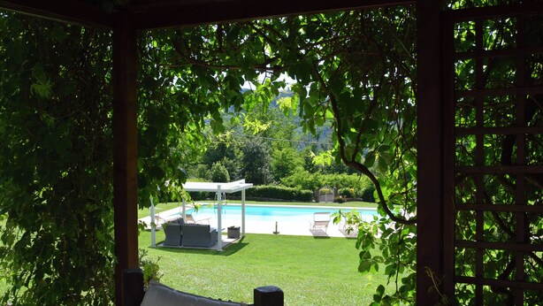 Un espacio al aire libre cubierto con piscina, sillones de descanso y una pérgola.