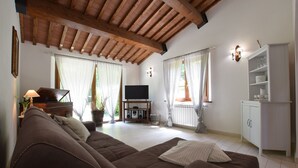 Una sala de estar con un sofá marrón, vigas de madera en el techo, un mueble para televisión y un armario.