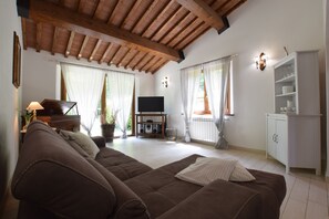 Ein Wohnzimmer mit braunem Sofa, Holzbalkendecke, einem Fernsehschrank und einem Schrank.