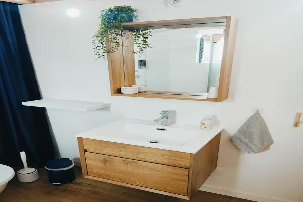 Un baño con tocador de madera, un lavabo blanco, un espejo, un perchero para toallas y una planta en maceta.