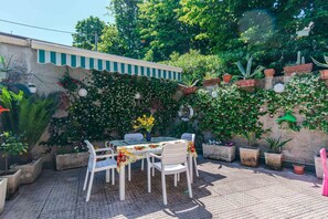 Eine Außenpatio mit Tisch und Stühlen, umgeben von Topfpflanzen und einer Wand mit Kletterpflanzen.