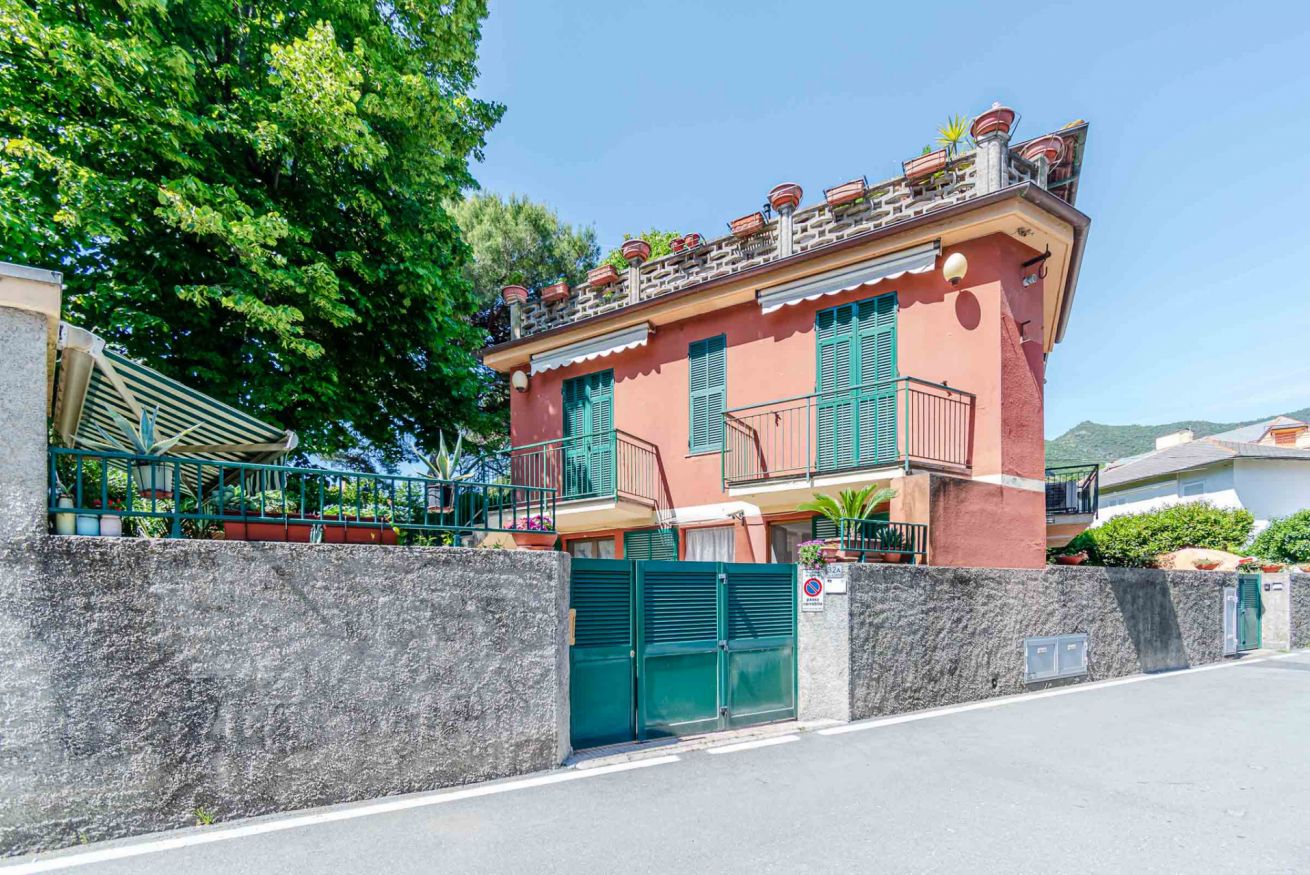 A two-story building with a red facade, green shutters, and a gated entrance.