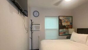 Quarto de hotel com uma cama, relógio, ventoinha no teto e um quadro na parede.