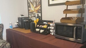 Uma mesa com micro-ondas, máquina de café e uma bandeja de lanches.