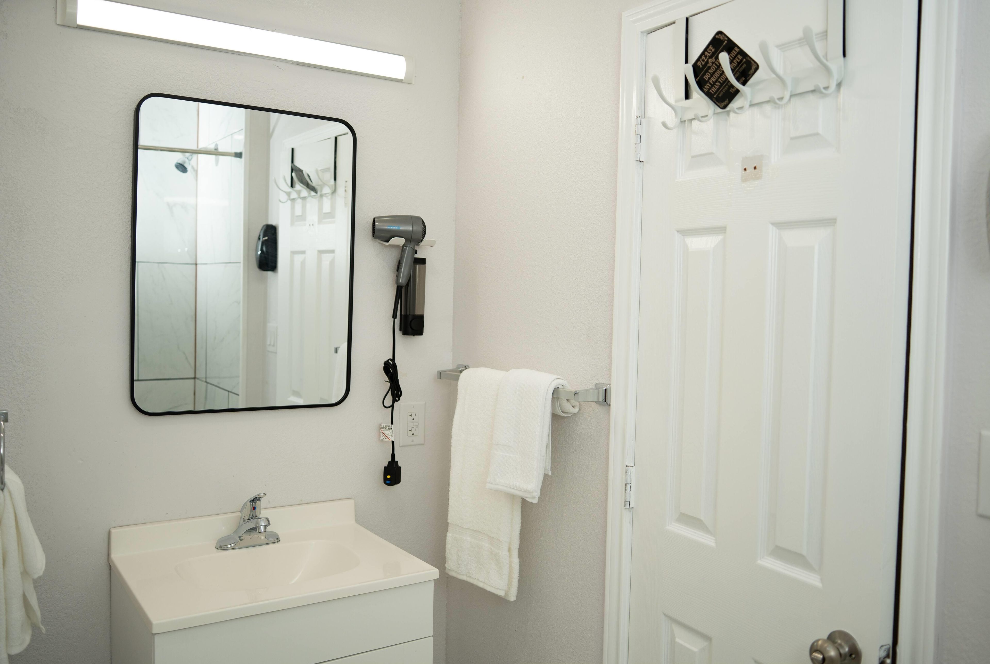 A bathroom with a white sink, a mirror, a hairdryer, a towel rack, and a door.