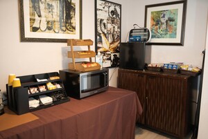 Una kitchenette con microondas, cafetera y una cesta de fruta sobre una mesa.