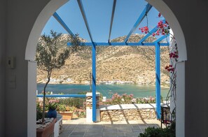 A view through an arched doorway with a blue structure, overlooking a coastal landscape with hills and a body of water. - Panorama rooms (Sifnos)