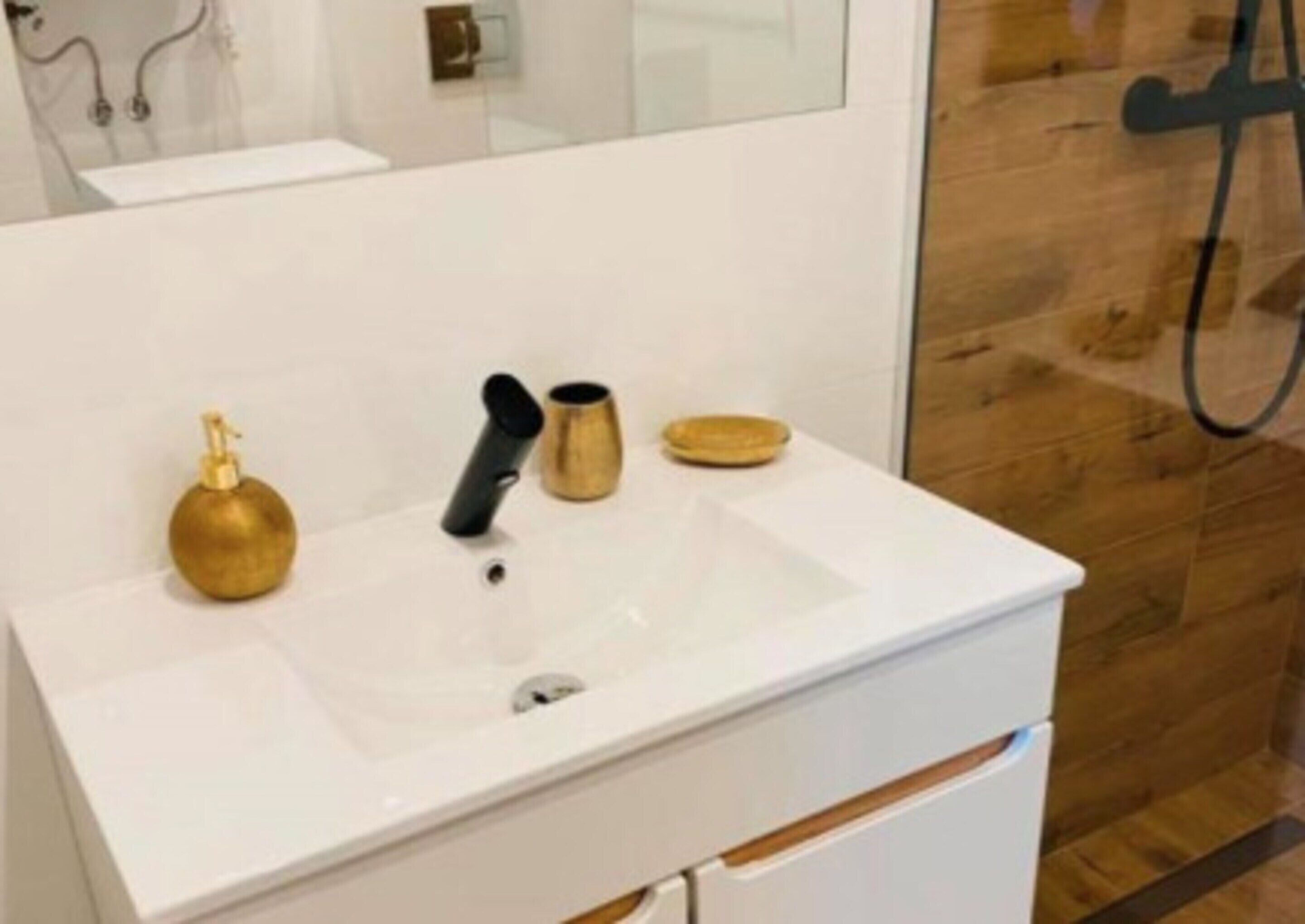 A white bathroom sink with a black faucet, a gold soap dispenser, and a brass cup.