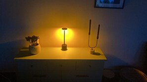 Un taulell al costat del llit amb una làmpada, una petita planta en test i un telèfon fixat a la paret.