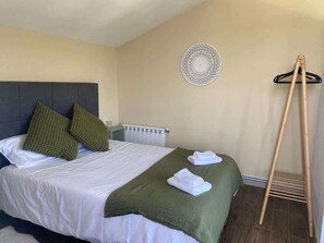 Uma cama bem arrumada com almofadas, um radiador, uma decoração circular na parede e um varal de madeira.