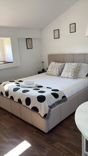 Quarto com cama, mesa de cabeceira, abajur e janela.