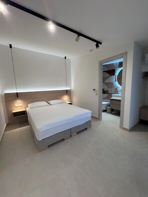 Ein modernes Schlafzimmer mit einem Bett, Nachttischen und einem durchgehenden Tür sichtbar erkennbaren Badezimmer.