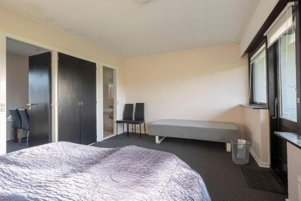 A bedroom with a bed, a chair, a desk, and a window.
