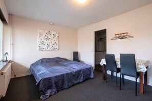 A bedroom with a bed, a desk, a chair, a table, and a hanging clothes rack. - Feriehuset Brøns (Skærbæk)
