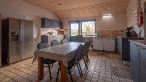 Eine Küche mit Esstisch, Stühlen, einem Kühlschrank, Schränken und einem Fenster.