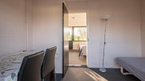Ein Zimmer mit einem Bett, einem Schreibtisch mit Stuhl, einer Stehlampe und einer Tür zu einem anderen Raum.