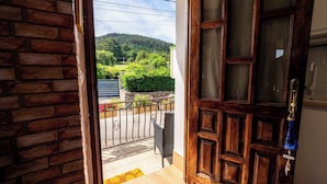 A wooden door leading to a balcony with a view of a green landscape and a parked car.