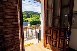 Una puerta de madera que da a un balcón con vistas a un paisaje verde y un coche estacionado.