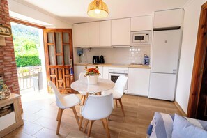 A modern kitchen with white cabinets, a dining table with chairs, and a view of greenery outside.