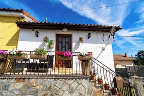 Un edificio blanco con una puerta marrón, escalones de piedra y barandillas metálicas.